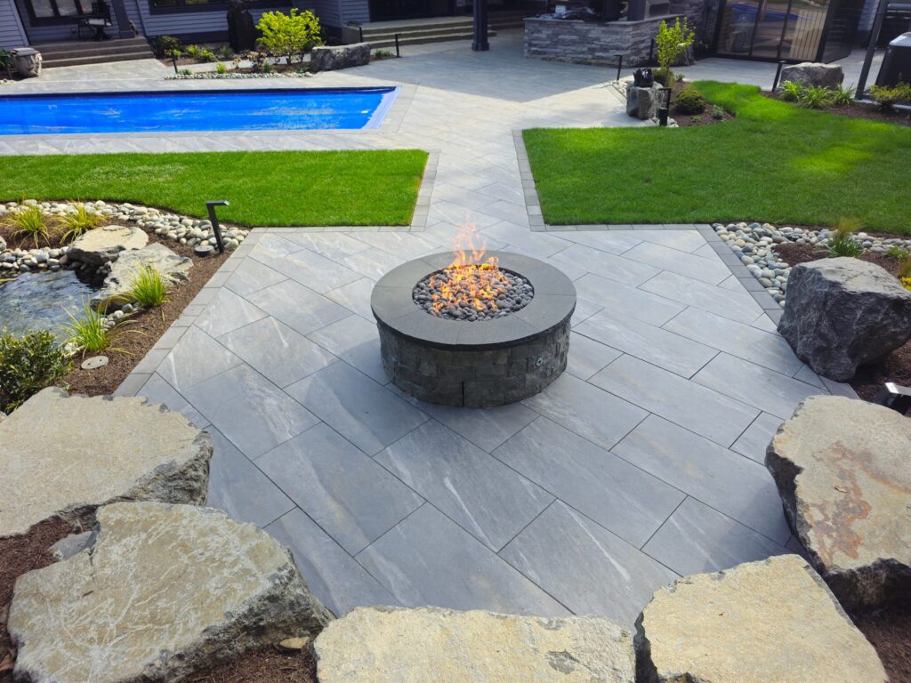 Round gas fire pit centered on a herringbone paver patio next to a pool in Bellevue