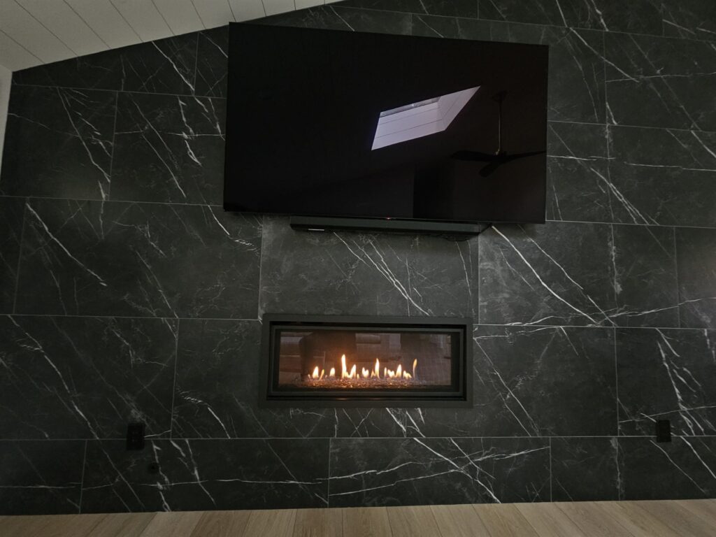 Modern linear gas fireplace set into a full-height black marble feature wall below a wall-mounted television