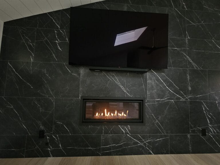 Modern linear gas fireplace set into a full-height black marble feature wall below a wall-mounted television