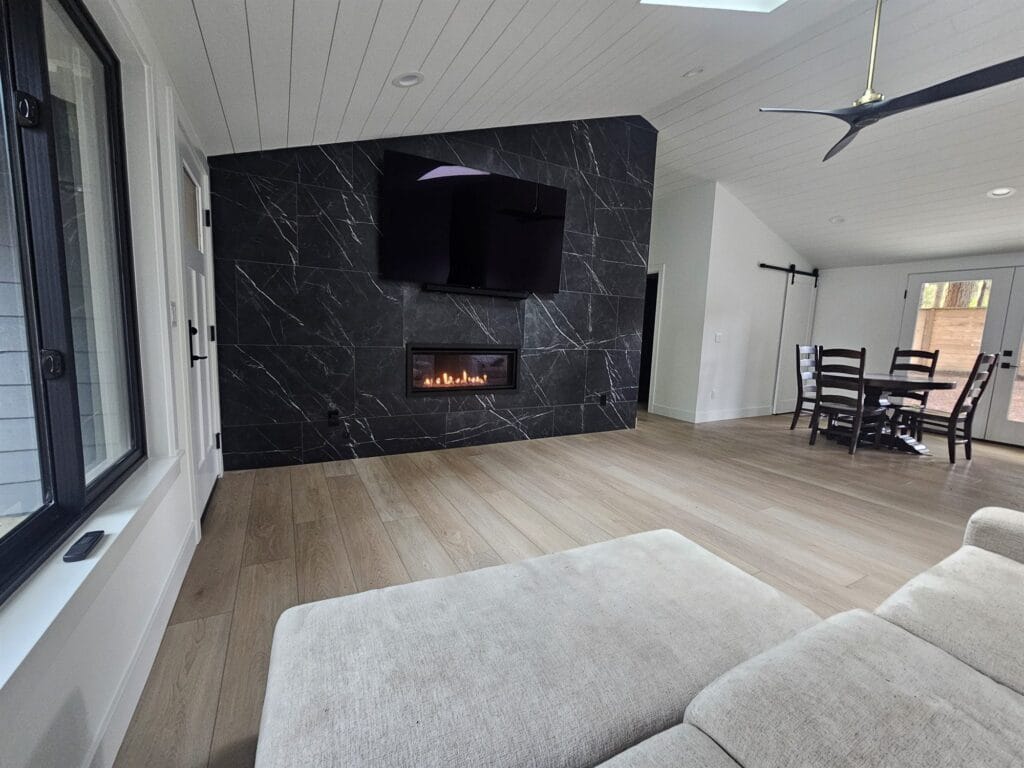 Linear gas fireplace set into a black marble-look tile wall below a TV in a bright open living room