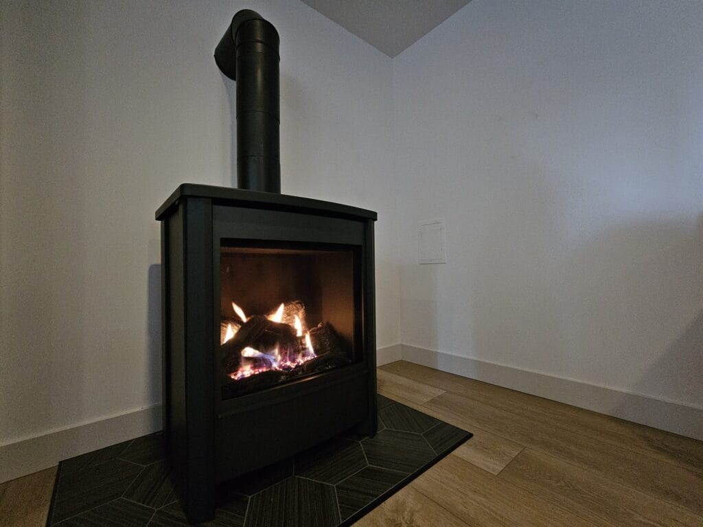 Black freestanding gas stove with a log set and black vent pipe on a tile hearth pad