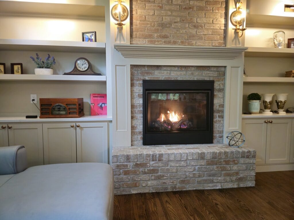 Gas fireplace in a whitewashed brick surround with a raised brick hearth, framed by white built-in shelves and cabinets