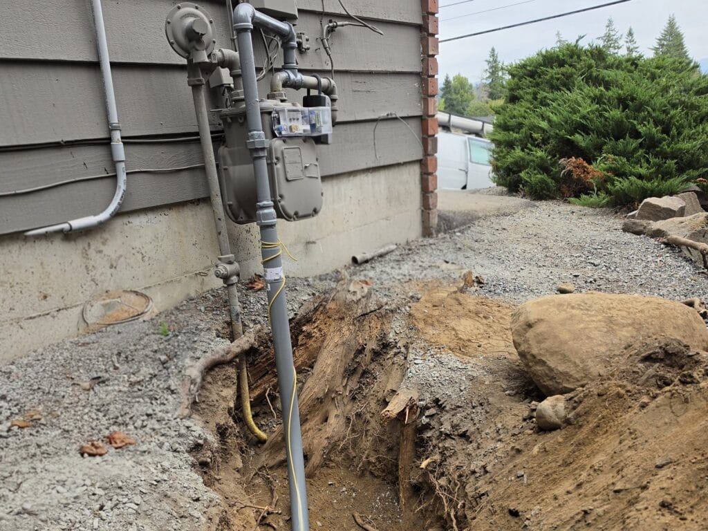 Gas meter and riser on the side of a home, with a fresh trench dug for a new underground gas line