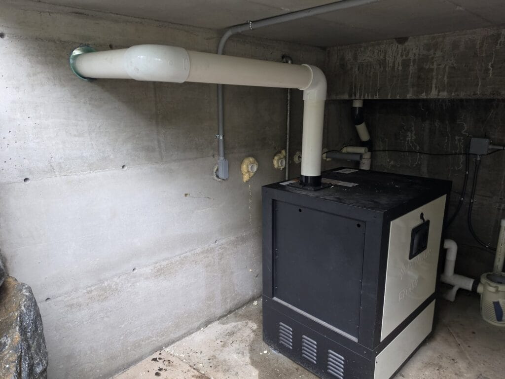 Gas pool heater with its white vent pipe in a concrete pool equipment room