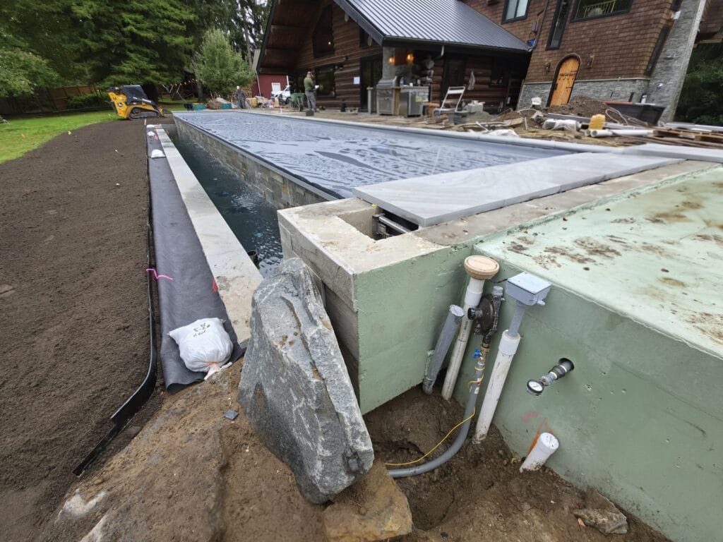 Gas line and conduit coming up beside the concrete wall of a new pool at a log home in Maple Valley