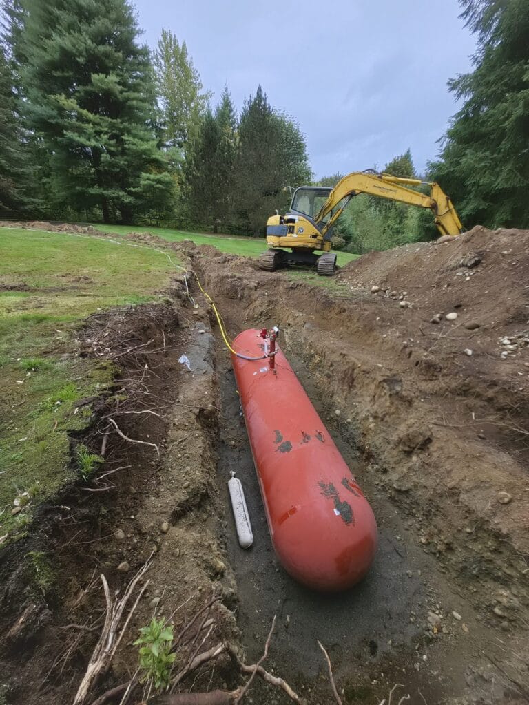 Looking down a trench at a red propane tank with the yellow gas line connected at its dome