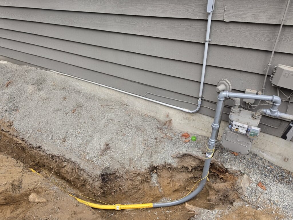 Yellow polyethylene gas line in an open trench, connected through a riser to the gas meter on a home