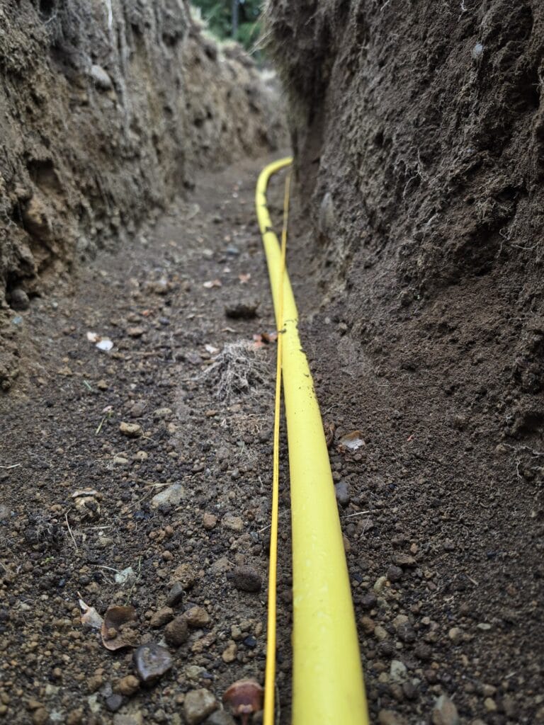 Yellow polyethylene gas line with tracer wire laid along the bottom of a deep trench